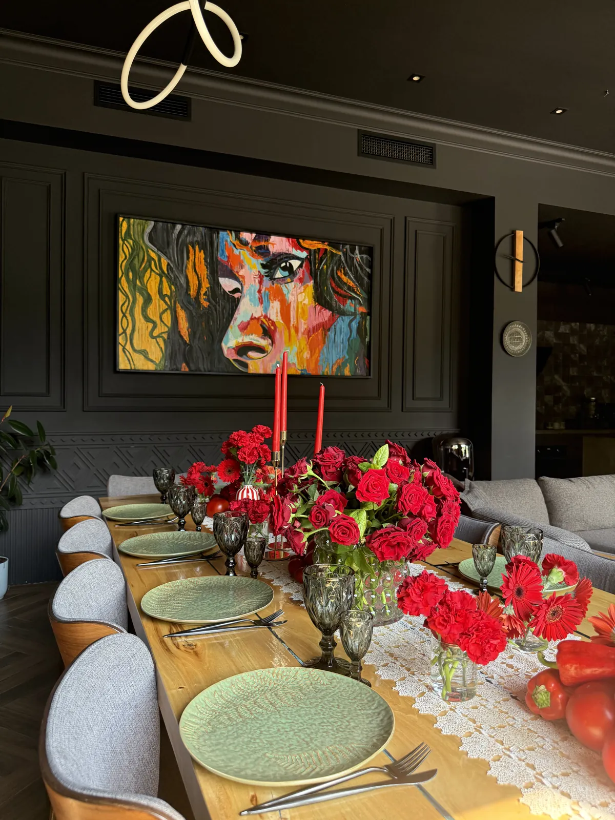 Long wooden table set with red roses, carnations and candles in the dining room, beneath a colourful painting