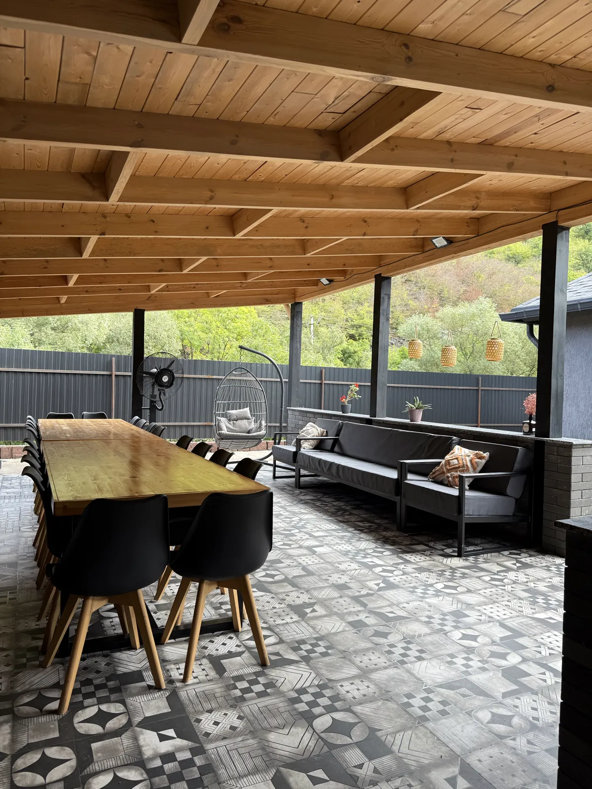 Covered gazebo with a long wooden table, sofas and a view of green hills