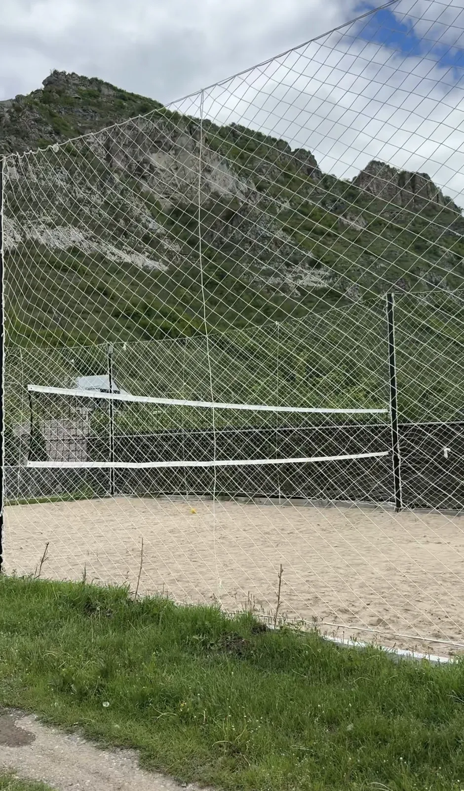Sand volleyball court with its net against a green mountainside