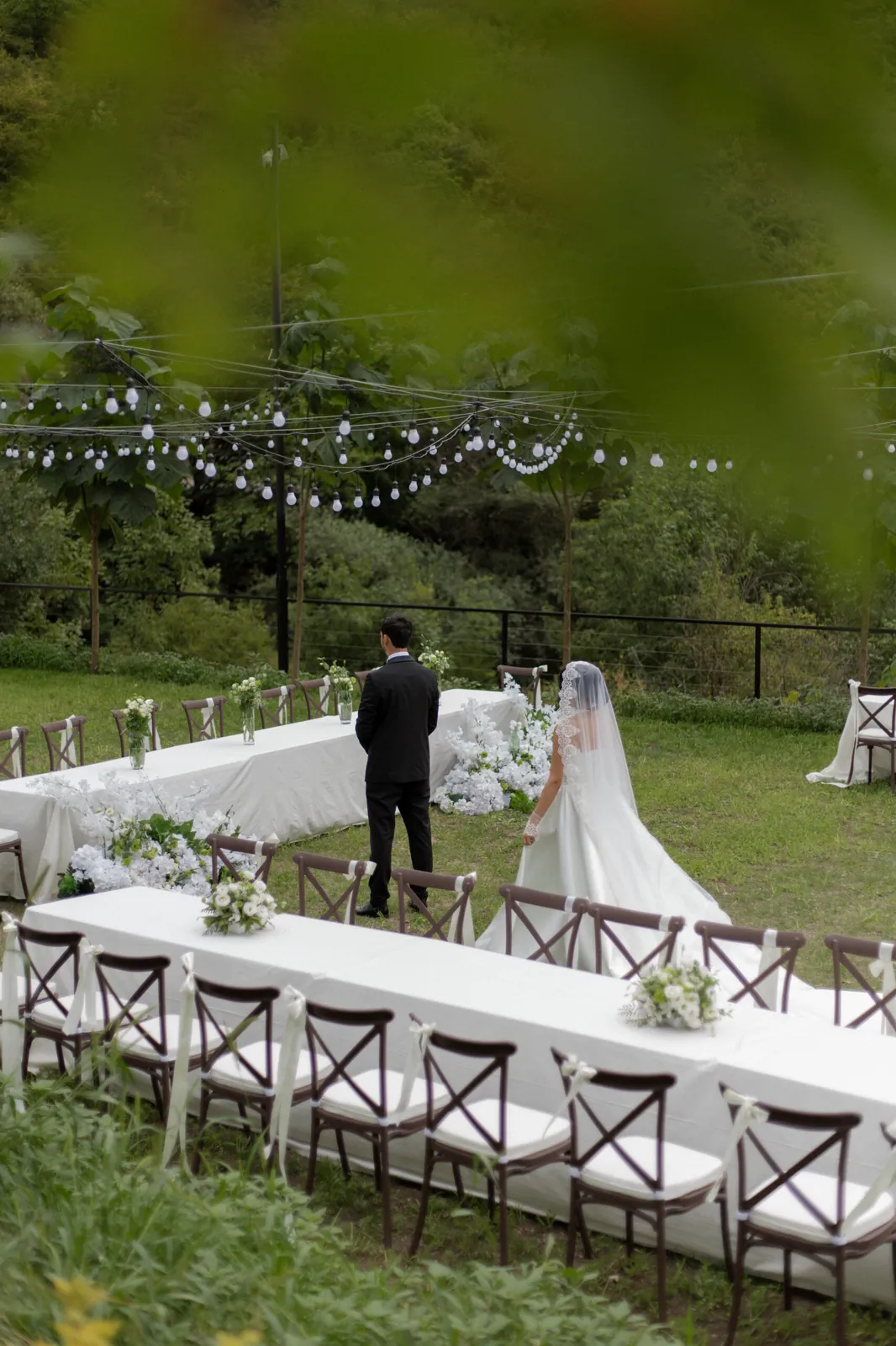 Bride and groom at an outdoor ceremony beside tables decorated with white flowers